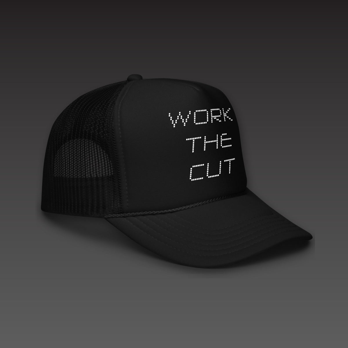 Scoreboard Trucker in black, WORK THE CUT stacked in white scoreboard dots on the front, seen from the side